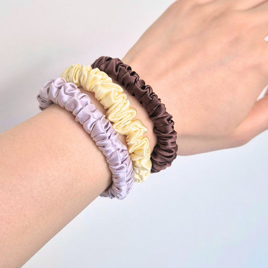 Three scrunchies in purple, yellow, and brown on a wrist against a light gray background